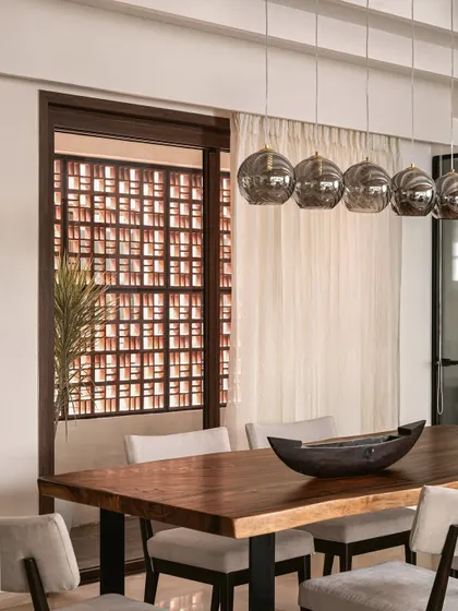 The dining area features a large wood table and smoked glass pendant lights. A terracotta jali screen provides privacy while allowing light to filter through, adding a beautiful, earthy detail.