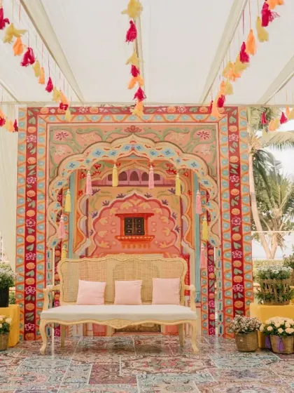 The main seating area for a Haldi ceremony, featuring a stunning custom-printed backdrop inspired by Rajasthani architecture and vibrant tassel hangings.