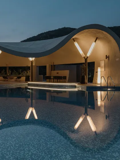 As dusk settles, the architectural lighting transforms the Aqua Pool & Spa into a dramatic and inviting space. The lights are designed to accentuate the unique V-shaped columns and the building's organic curves.