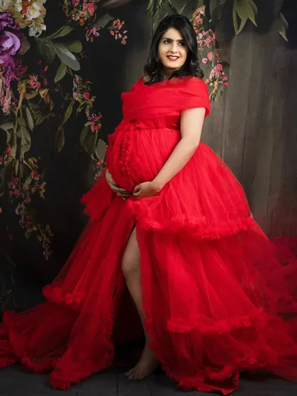 A vibrant and joyful portrait of a mom-to-be in a stunning red ruffled gown. The floral backdrop adds a touch of romance and drama.