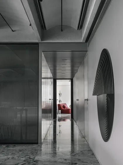 A transitional space in the Vaulted Haus. The polished grey marble floor reflects the vaulted ceiling and sculptural wall art, demonstrating how material choice can enhance the perception of light and space in a narrow passage.