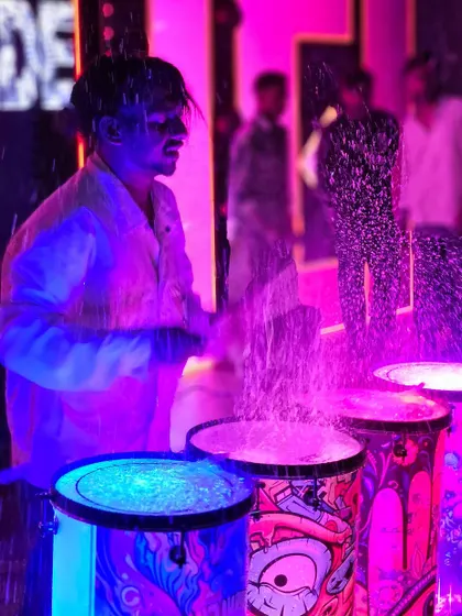 Another shot of the liquid drum performance, with water splashing high into the air under the vibrant stage lights.