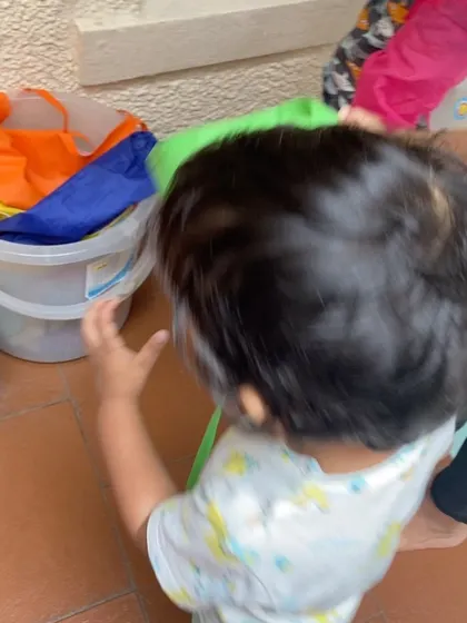 A child helps put away colorful play silks into a bucket. This sorting and organizing task is a simple way to practice categorization and responsibility.