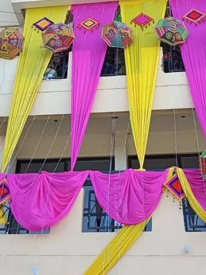 Balcony decoration featuring pink and yellow drapes accented with colorful hanging umbrellas and props.