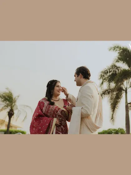 A sweet, candid moment where the groom gently touches the bride's cheek, set against a backdrop of palm trees. This frame captures a simple, loving gesture that tells a story of long-lasting love.