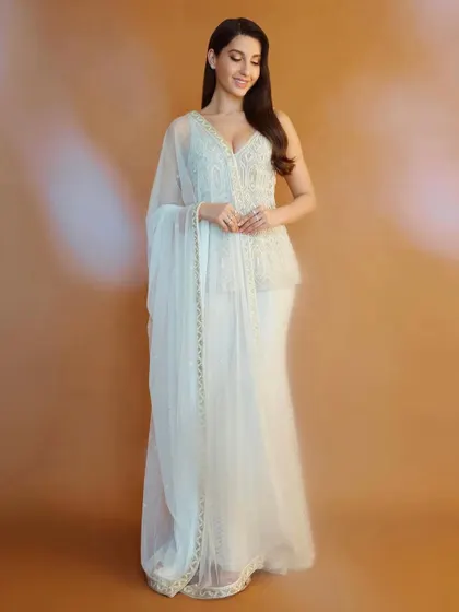 Nora Fatehi looks ethereal in this white peplum and sharara set by Ritika Mirchandani. This is a great example of fusion wear, blending traditional embroidery with a modern silhouette for a chic, celebratory look.