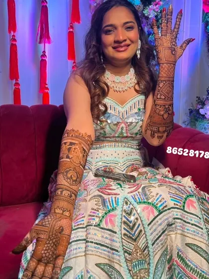 A happy bride in a beautiful lehenga, showing off her full-arm story-telling mehndi.