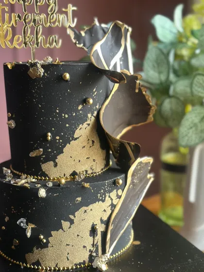 Bold, beautiful, and dipped in gold. This black and gold two-tiered cake, designed for a retirement party, makes a luxurious statement with its abstract sails and gold splatter.
