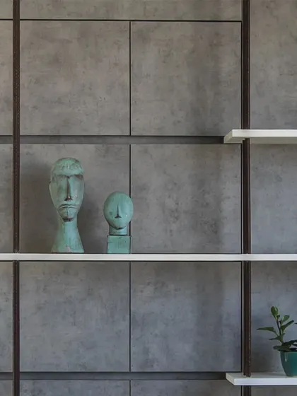 Detail of a shelving system in the 'Acutely Bare' office, where thin white shelves are set against a grid of concrete panels and rebar, blending industrial and minimalist elements.