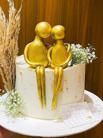 An elegant anniversary cake featuring a golden couple figurine and a calendar marking their special date. The delicate baby's breath adds a touch of romance to this heartfelt design.