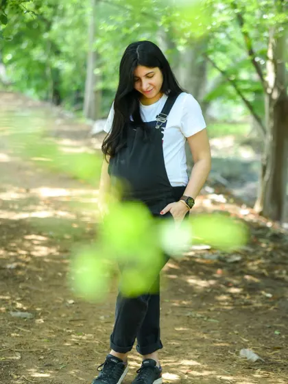 A candid and natural portrait of a mom-to-be in black dungarees, enjoying a quiet moment in the woods. The foreground leaves add a nice artistic touch.