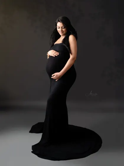A gentle and serene solo portrait. The soft lighting and the way she is cradling her bump create a feeling of peace and love in this black gown shot.