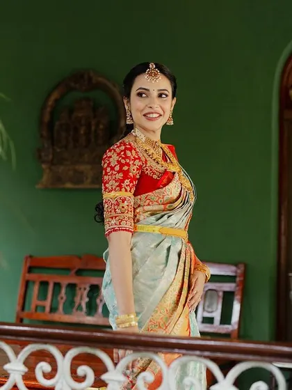 A bride on a balcony, her beautiful saree and jewelry pop against the rich green wall and traditional architecture.