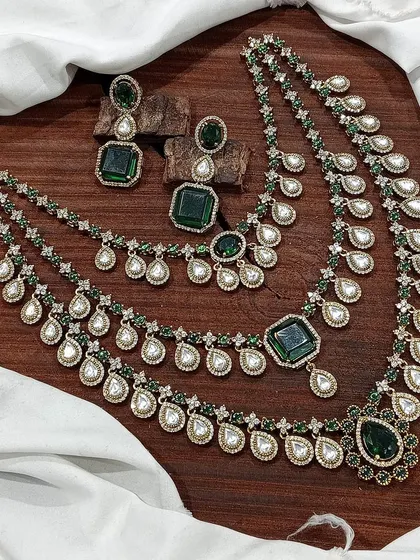 A grand, three-layered AD necklace set. This piece is designed for maximum impact, featuring square and teardrop stones, and is available in blue, green, pink, and red.
