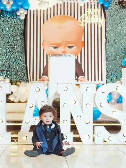 A solo shot of the birthday boy amidst his party's awesome decor. This photo highlights both the child and the fantastic "Boss Baby" themed setup with his name in lights.