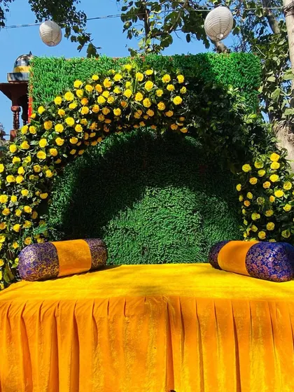 A simple and elegant Haldi seating idea, with a lush green backdrop accented by an arch of bright yellow flowers.