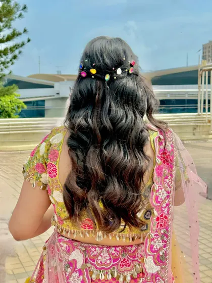 A playful and colorful hairstyle for a mehendi, with soft waves and multi-colored gem accessories.