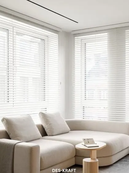 A bright and airy living room corner where a plush, light-colored chaise lounge offers a perfect spot for relaxation, complemented by minimalist furniture and clean white blinds.