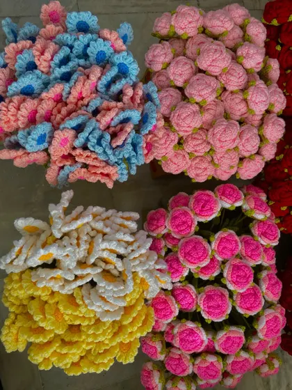 Piles of colorful crochet flower heads, including daisies and roses, waiting to be assembled into stems.