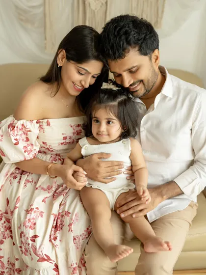 A picture-perfect family of three. The parents lovingly hold their daughter, who is sitting on her father's lap, creating a classic and beautiful family portrait.