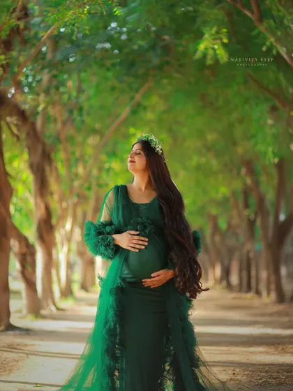 A serene outdoor portrait in a green gown. The mother-to-be is captured in a moment of quiet connection with her baby, surrounded by nature.
