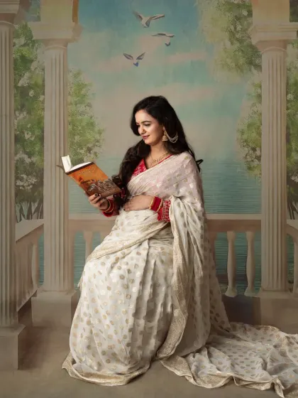 A peaceful, scenic portrait. The mom-to-be reads a book against a painted backdrop of a seaside balcony, creating a calm and imaginative scene.
