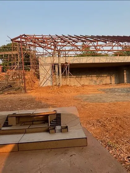 A view of the steel roof structure being erected for the yoga retreat's stage pavilion. In the foreground is a physical model used to explain the complex design to the site team.