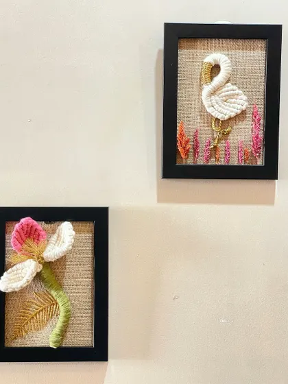 A set of two framed macrame art pieces. One features a graceful swan, and the other a beautiful blooming flower, both set against a natural burlap background.