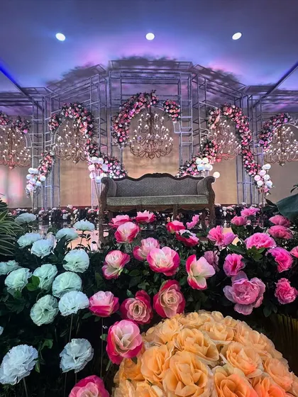 A romantic reception stage featuring a metal framework adorned with pink and white flowers and elegant chandeliers.