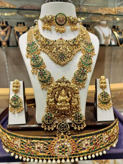 A grand Lakshmi-themed bridal set with green and red stones. This set includes a choker, a long haram, and a matching vaddanam.