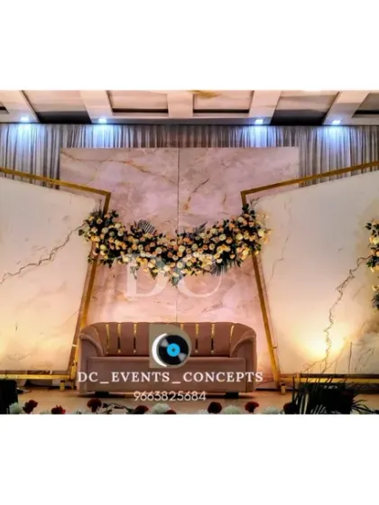 This modern wedding reception stage features a clean, elegant design with marble-finish backdrops, geometric gold frames, and asymmetrical floral arrangements for a sophisticated look.