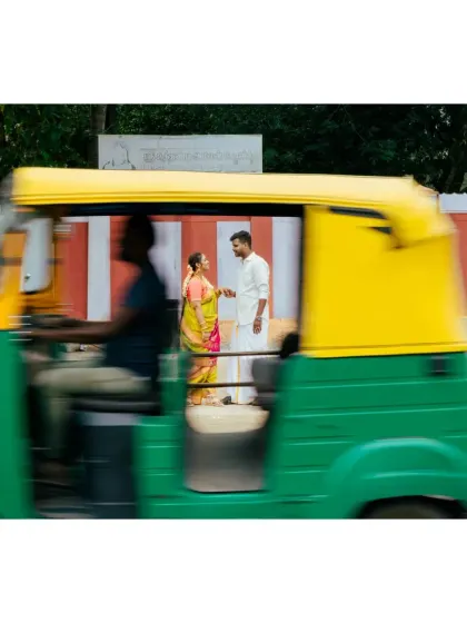 A creative shot using motion blur, capturing a couple's quiet moment on a busy street with an auto-rickshaw speeding by. It freezes their world in time.