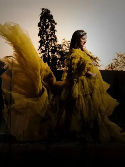 The flowing fabric of this yellow ruffled gown creates a beautiful, dynamic shape against the evening sky. It's a perfect choice for capturing artistic and memorable maternity shots.