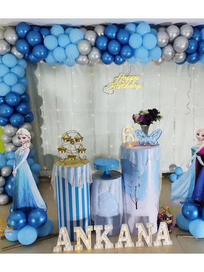 A magical Frozen-themed birthday party for a 6-year-old, featuring a blue and silver balloon arch, character cutouts of Elsa and Anna, and a winter-themed backdrop.