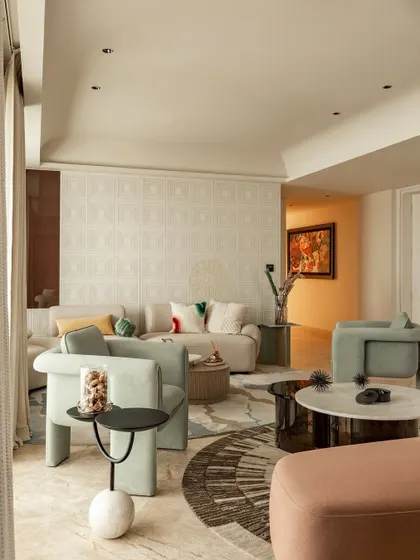 We used sculptural armchairs in a soft sage green to create an inviting conversation area. The layered rugs and mix of circular and organic shapes in the furniture add a playful, modern touch to this elegant living space.