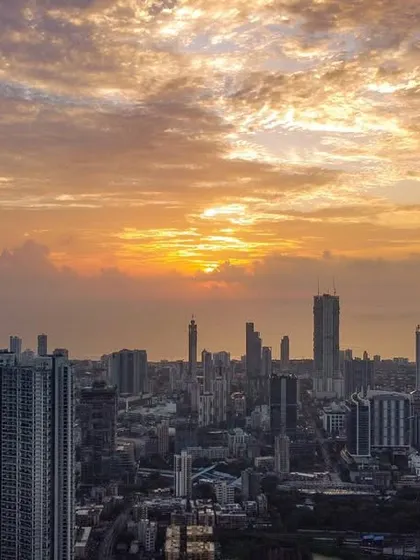 A wider view of a dramatic, cloud-filled sunset over the Mumbai cityscape, showing more of the urban landscape.