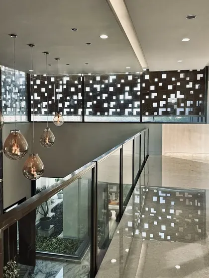 An interior corridor where a perforated screen creates a captivating play of light and shadow. The light filtering through the geometric pattern animates the space, while pendant lights add a warm glow.