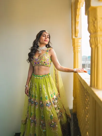 A stunning solo portrait of the bride in her vibrant green and yellow lehenga, basking in the sunlit glow of her Haldi day.