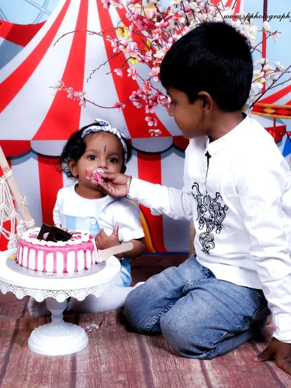 A cake smash session is a fun way to celebrate a first birthday. This shot captures a sweet moment between siblings as the older brother helps his little sister taste the cake.
