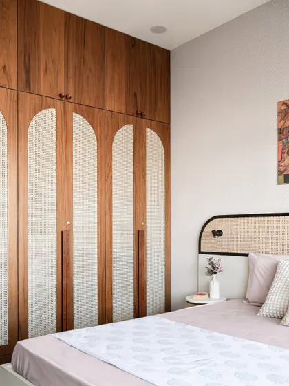This bedroom features a beautiful custom wardrobe with arched cane panels and wood finishing. The design is a perfect blend of modern and traditional elements, creating a warm and personalized space.