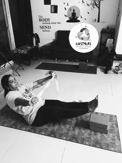 A client uses a yoga strap to assist with a core and leg strengthening exercise, demonstrating how props can add challenge and support.