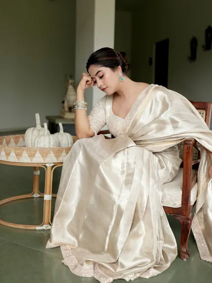 A seated portrait in the ivory tissue silk saree, conveying a mood of quiet luxury and timeless grace.