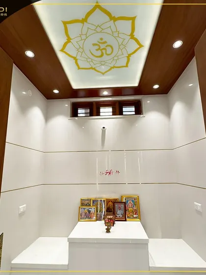 A minimalist and modern puja space with a beautiful lotus and 'Om' motif on the backlit ceiling. The clean white tiles and simple wooden frame create a serene and peaceful environment.