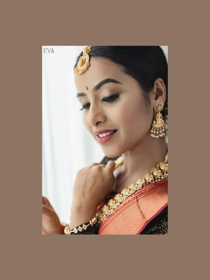 A close-up beauty shot with a soft, dreamy feel. The focus is on the model's delicate features, the maang tikka, and jhumka earrings, framed with a brown border for an artistic touch.
