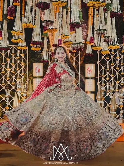 A happy bride twirls in front of a traditional stage, showcasing her beautiful lehenga against the backdrop of intricate decor and hanging florals.