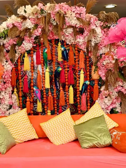 A closer look at the Mehendi seating area. The backdrop is a burst of colour with multi-hued tassels, pampas grass, and florals, complemented by comfortable cushions for the bride and groom.