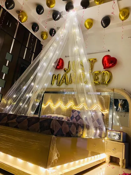 The reflection in the mirrored wardrobe shows the full effect of the black and gold balloons and the glowing canopy in this wedding night setup.