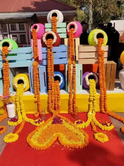 A creative and artistic floral installation for a Mehendi or Haldi event, with marigold garlands appearing to flow out of colorful pots.