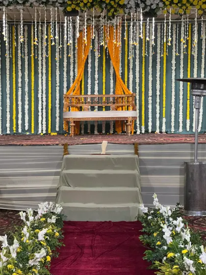 A traditional wooden swing (jhoola) placed on the stage for the Haldi ceremony. The backdrop features strings of white and yellow flowers.