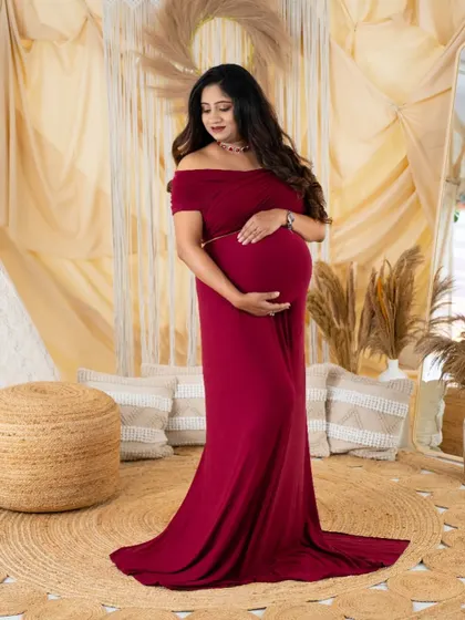 A full-length portrait of a mom-to-be in a beautiful deep red gown. The simple elegance of the dress is highlighted in our boho studio setting.